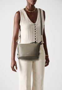 Borsa a tracolla in pelle verde oliva con una texture liscia, tracolla regolabile e dettagli in metallo dorato. Presenta il logo del brand sul davanti.