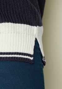 Marinblå och vit stickad tröja med ribbad textur, sidoflikar och kontrasterande ränder vid fållen. Mjuk material.