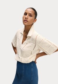 Haut tricoté à manches courtes de couleur crème avec un col en V et un motif carré texturé ; associé à une jupe en denim taille haute.