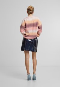 Meerkleuren gebreide trui met roze, oranje en witte strepen, gecombineerd met een glanzende zwarte vinyl mini-rok. Lichtblauwe hakken.