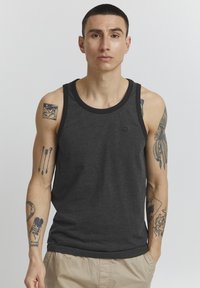 Débardeur gris avec un bord noir, fabriqué en matériau doux. Présente un petit logo sur la poitrine et expose des tatouages sur les bras du modèle.