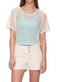 Witte mesh cropped top met een ronde halslijn, met een teal onderlaag. Gecombineerd met lichtbeige denim shorts, opgerold aan de mouwen.
