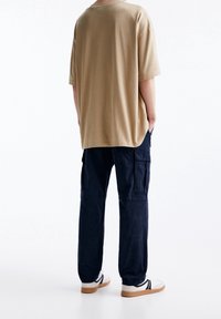 Beige katoenen oversized t-shirt gecombineerd met marineblauwe cargobroek, met zijzakken en elastische manchetten, aangevuld met witte sneakers.