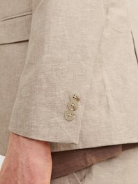 Světle bežová lněná saka s rukávem, který má čtyři světle hnědé knoflíky a viditelné švy. Hladká textura s jemným vzhledem měkké látky.