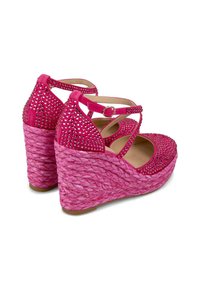 Sandales compensées roses avec une semelle tissée texturée, ornées de strass, dotées de brides croisées et d'une fermeture à boucle au niveau de la cheville.