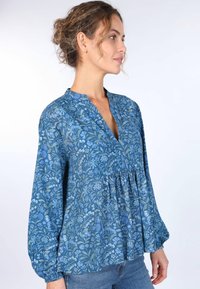 Helle, blaue Bluse aus leichtem Stoff, mit V-Ausschnitt, langen Puffärmeln und einer gerafften Taille, verziert mit einem verspielten botanischen Muster.