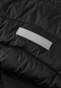 Giacca isolante nera con una texture liscia e lucida. Etichetta grigia piatta ben visibile con cuciture sulla parte anteriore, che presenta la scritta "name it."