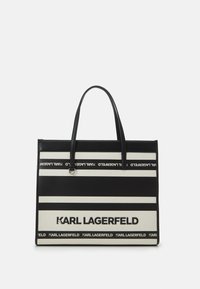 Sac cabas en noir et blanc à rayures horizontales, fabriqué en toile. Dispose de poignées robustes et de détails avec logo.