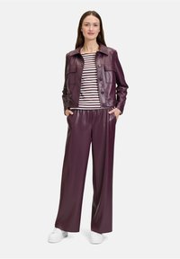 Violet faux leren jas met knoopsluiting en twee borstzakken, gecombineerd met bijpassende losse broek en een gestreept shirt. Witte sneakers.