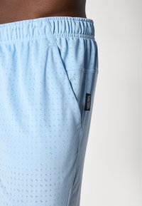 Light blue athletic shorts with a textured pattern, elastic waistband, and side pockets. Features a small tag on the seam.
