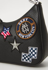 Geantă de mână din piele neagră, cu diverse patch-uri brodate, inclusiv stele și un logo circular cu textul "DKNY NEW YORK CITY".