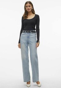 Maglietta nera a maniche lunghe con scollo rotondo, abbinata a jeans a vita alta larghi di colore azzurro chiaro e décolleté crema a punta.