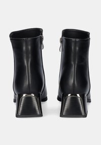 Botines negros hechos de cuero suave, con un tacón cuadrado con un acabado plateado brillante y una cremallera lateral para el cierre.