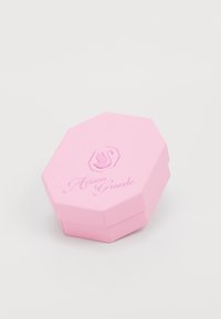 Boîte octogonale rose avec surface texturée. Présente un logo en relief et le nom "Ariana Grande" dans une police décorative à l'avant.