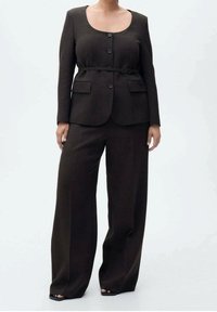 Brauner maßgeschneiderter Blazer mit rundem Ausschnitt, zwei Knöpfen und tailliertem Gürtel, kombiniert mit weit geschnittenen braunen Hosen. Glatte Textur, ohne Muster.