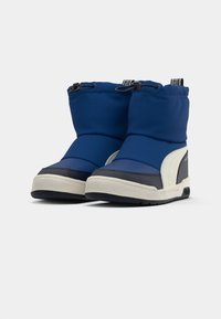 Bottes isolées bleues avec une texture lisse, présentant un accent blanc, une semelle en caoutchouc et un haut élastique ajustable pour un ajustement sécurisé.
