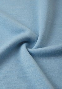 Jasnoniebieska tkanina o gładkiej, miękkiej fakturze, prezentująca wzór dzianiny, delikatnie układająca się w fałdy. Brak wyraźnych akcentów czy elementów metalowych.