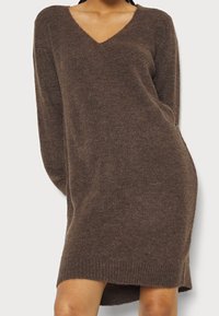 Robe-pull marron en maille avec encolure en V, manches longues et ourlet côtelé. Texture douce et coupe décontractée, tombant au-dessus de la mi-cuisse.