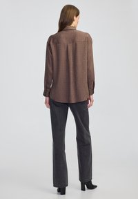 Bruine overhemd met knopen en een structuurpatroon, lange mouwen en een kraag, gecombineerd met zwarte rechte broek en zwarte hielboots.