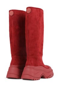 Stivali alti in suede rosso con una suola spessa in gomma e design texturizzato. Presentano accenti con logo rotondo vicino alla parte superiore.