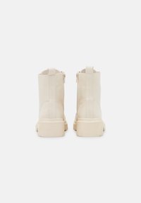 Bottines en cuir crème avec une texture lisse, un design minimaliste, une fermeture à glissière sur le côté, et une semelle robuste légèrement surélevée.