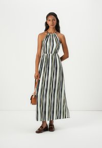 Maxikjole med vertikale striper i grønn, svart og hvit. Halterneck, innsvingt midje og løs skjørt. Modell som holder en brun veske.