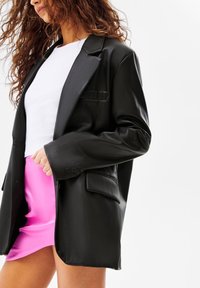 Černý blazer z umělé kůže s jednou náprsní kapsou, velkými klopami a knoflíky na manžetách, doplněný bílým ribbovaným topem a růžovou mini sukní.