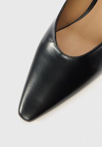 Czarny skórzany but na wysokim obcasie z zaostrzonym noskiem i gładką fakturą. Wnętrze jest koloru jasnobrązowego, z niskim wycięciem.