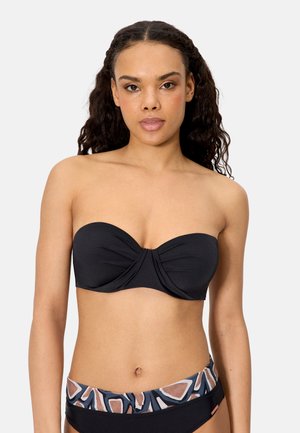 Mujer con cabello rizado, vistiendo un top de bikini negro sin tirantes y una parte inferior de bikini negra con cinturilla estampada.