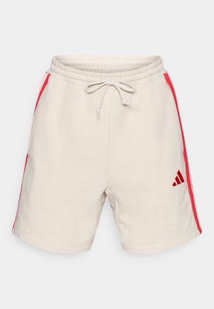 Beige sweatshorts met rode zijstrepen, elastische tailleband, trekkoord en een geborduurd zwart logo. Zachte textielstructuur.