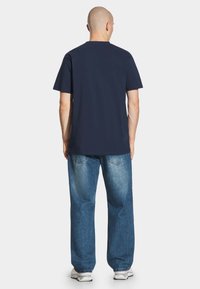 Granatowa bawełniana koszulka z krótkim rękawem i okrągłym dekoltem, połączona z luźnymi, jasnoniebieskimi dżinsami i białymi trampkami.