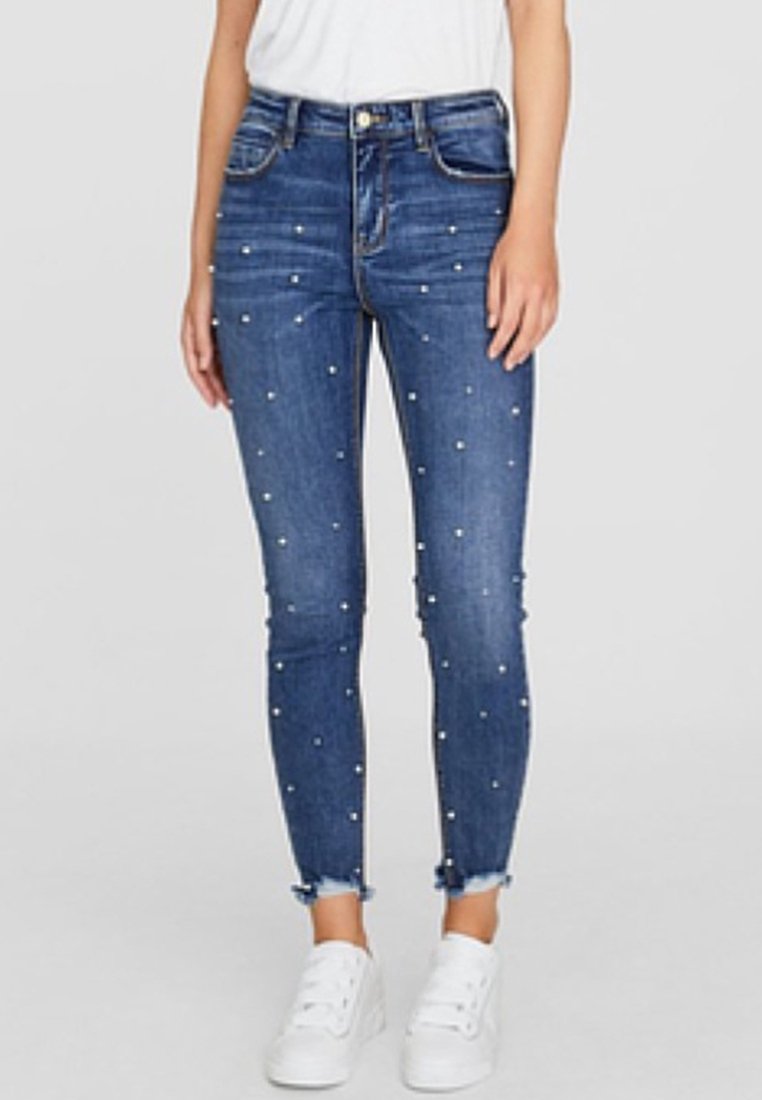 Slim jeans i mörkblå denim, prydda med små vita pärlor, med fransad nederkant och femficksdesign. Bärs med vita sneakers.