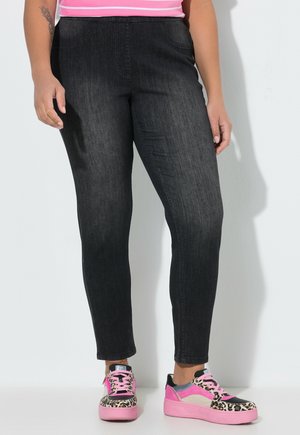 Beine in eng anliegenden schwarzen Jeans und bunten Plateausneakern mit pinkfarbenen Schnürsenkeln und Leopardenmuster-Akzenten.