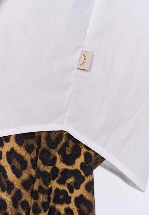 Biała koszula o subtelnej teksturze, z dołem wykończonym beżową metką; połączona z brązowym i czarnym materiałem w panterkę poniżej.
