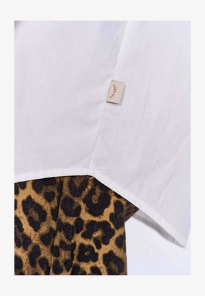 Biała koszula o subtelnej teksturze, z dołem wykończonym beżową metką; połączona z brązowym i czarnym materiałem w panterkę poniżej.