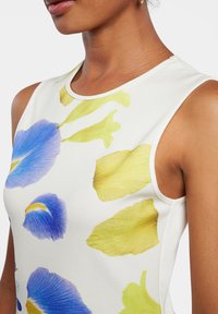 Haut sans manches en tissu blanc orné de grandes impressions florales bleues et jaunes, avec un col rond et une texture lisse.