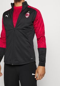 Black athletic jacket with red patterned sleeves, featuring a front zipper, logo, and "DRYCELL" branding at the hem.