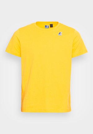 Żółta koszulka T-shirt z bawełny, z okrągłym dekoltem, krótkimi rękawami i małym niebieskim logo na lewej piersi. Gładka tekstura.