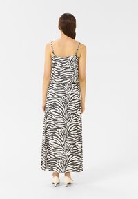 Maxikleid im Zebra-Streifenmuster; leichtes Material, Spaghettiträger, lockere Passform. Die Rückansicht zeigt das fließende Design und die Schuhdetails.