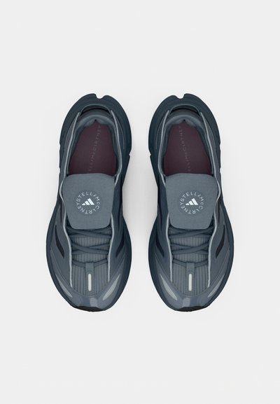 Σκούρα γκρι αθλητικά παπούτσια με αεροδυναμική σχεδίαση. Επάνω μέρος από υφασμάτινο υλικό με υφή, επενδεδυμένη γλώσσα και εμφανές λογότυπο στη γλώσσα. Ανακλαστικές λεπτομέρειες.