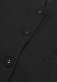 Crni sako s teksturiranim materijalom, četiri okrugla dugmeta sa srebrnim detaljima i strukturiranim reverima. Minimalistički dizajn s jednim dugmetom.