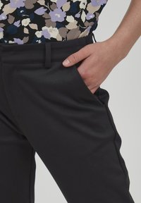 Mustad mustad püksid, millel on sile tekstuur ning küljetaskud. Sobiv disain täiendab lillemustriga ülemust.