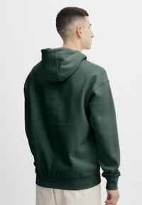Sudadera verde oscuro hecha de suave tela de mezcla de algodón. Cuenta con una capucha con cordón, puños y dobladillo acanalados, y tiene un diseño de corte relajado.
