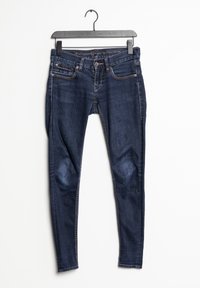 Jeans skinny de mezclilla azul con una cintura de mediana altura, diseño de cinco bolsillos, acentos cosidos y una textura suave, colgados en una percha negra.