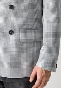 Gray and blue plaid blazer with a textured fabric, double-breasted design, black buttons, and a chest pocket on the left side.