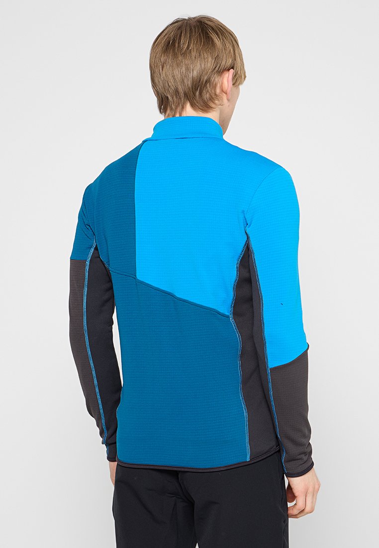 Camisa de manga larga azul y negra con un diseño geométrico, que presenta un tejido texturizado, colores contrastantes y detalles de costura visibles.