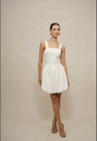 Fehér ujjatlan ruha négyzet alakú nyakkivágással, testhezálló felsőrész és bővülő szoknya. Simaságú anyag és minimalista design. Arany szandálok teszik teljessé a megjelenést.