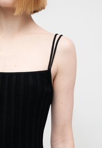 Μαύρο ριμπ αμάνικο τοπ με λεπτές τιράντες και τετράγωνο ντεκολτέ, κατασκευασμένο από απαλό ύφασμα με εφαρμοστή γραμμή.