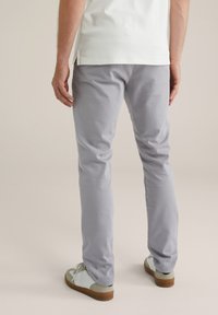 Pantalones slim-fit de color gris claro, en material de algodón, con una textura sutil y un acabado suave, combinados con zapatillas claras y una camisa blanca.