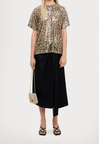 Hnědá halenka s leopardím potiskem a flitry, krátké rukávy, v kombinaci s černou sukní. Doplňky zahrnují malou korálkovou kabelku a černé sandály na pásky.